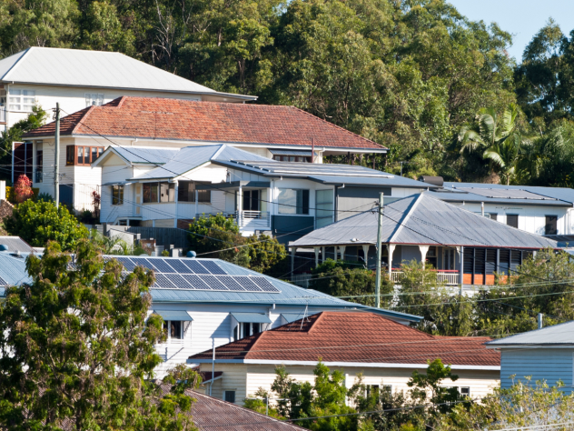 Photo of a row of houses in a sloping Queensland street, surrounded by trees. Some houses have rooftop solar, and are connected to the electricity network.