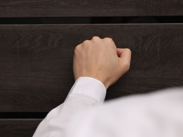 Photo of a person in a white shirt's arm, knocking on a door.