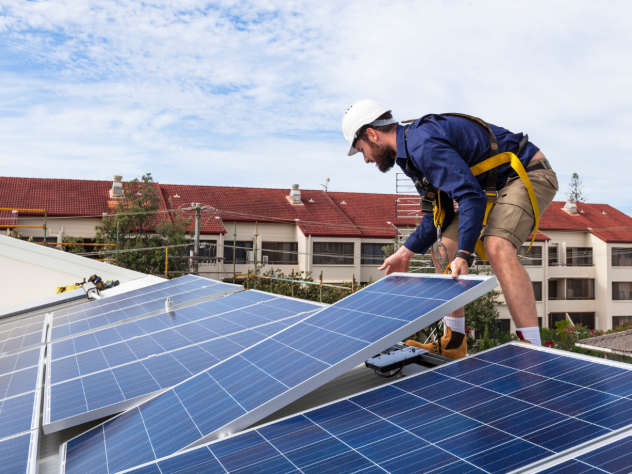 Photo of an electrician installing solar panels on a rooftop.