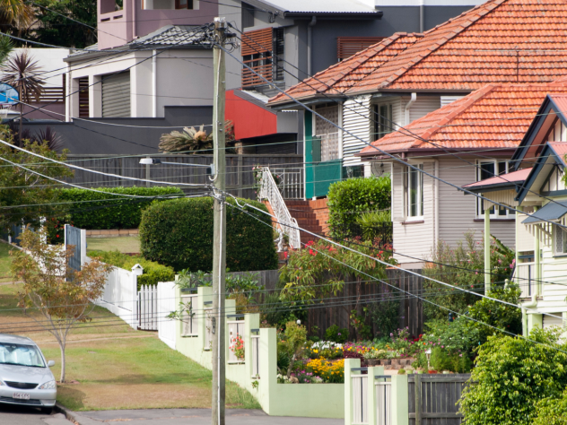 Photo of suburban Brisbane street, featuring power lines, a parked car and rows of houses.