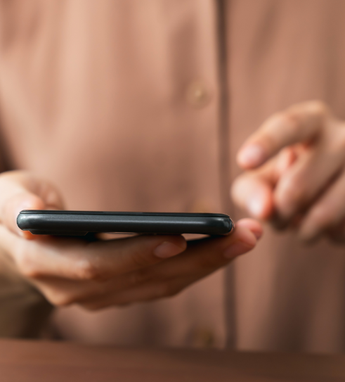 Close-up photo of a person in a brown, button-up shirt holding and tapping on a mobile phone.