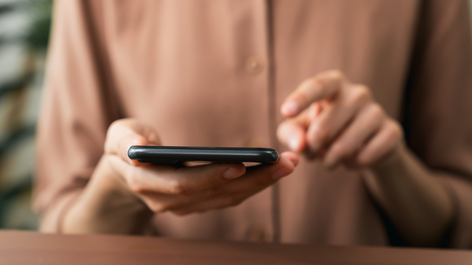 Close-up photo of a person in a brown, button-up shirt holding and tapping on a mobile phone.