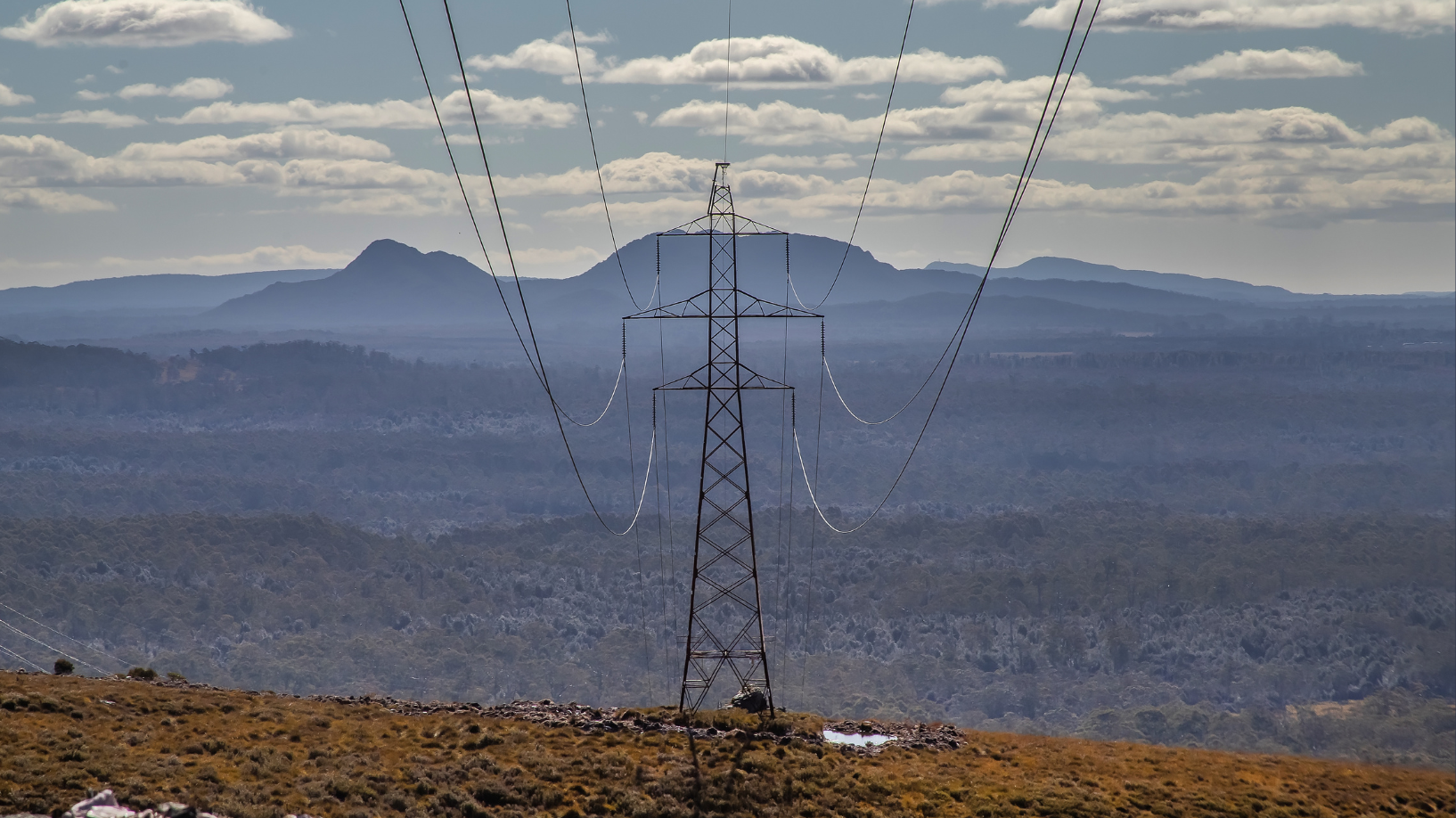 Photo of a transmission line with an Australian landscape and clouds in the background.