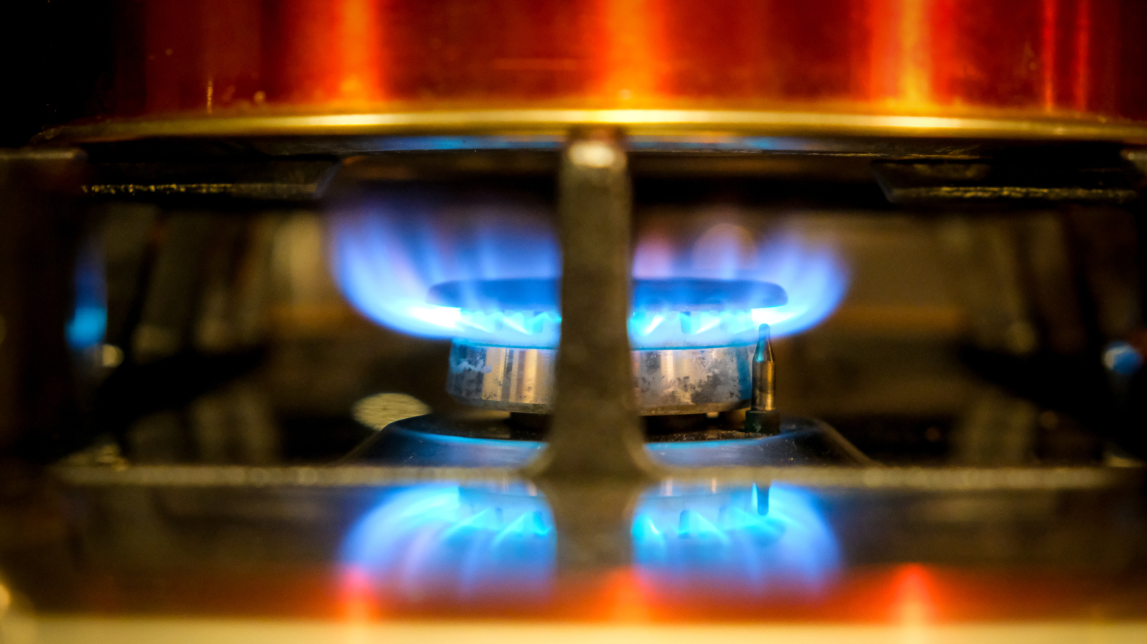 Close-up photo of a stovetop gas burner underneath a pot; the burner's flame is burning bright blue.