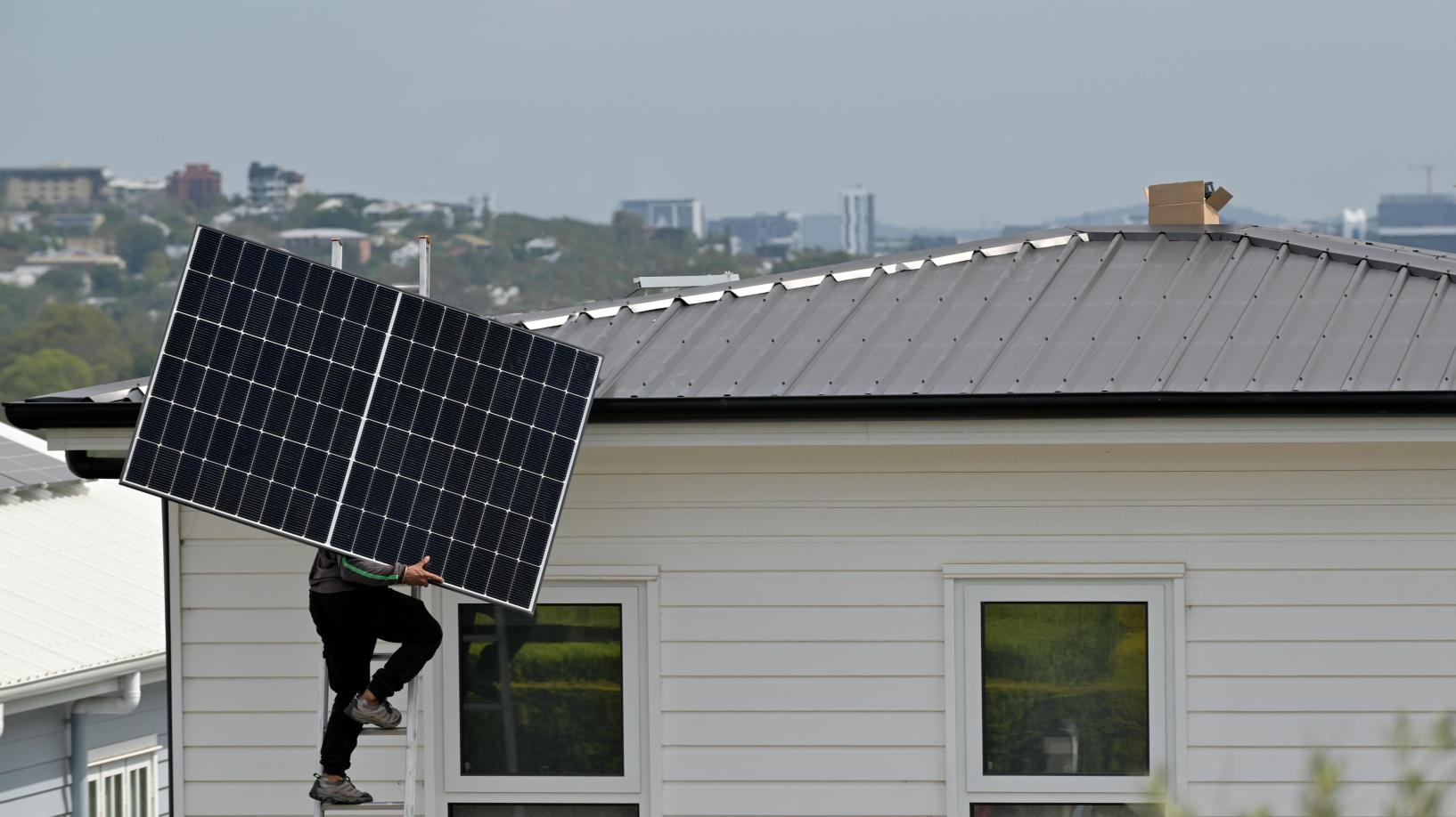 Photo of a person with a solar panel, standing on a ladder. They are going to install the solar panel on a rooftop.