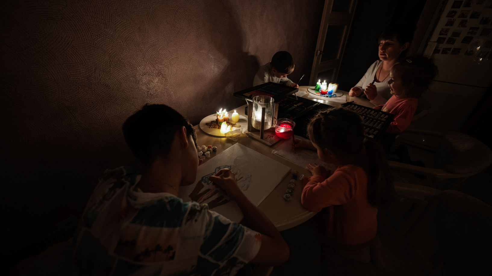 Family sitting at a table in the dark with candles illuminating their activities. 