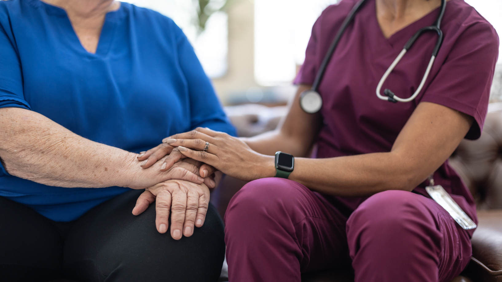 A doctor sits next to a patient and holds their hand. 