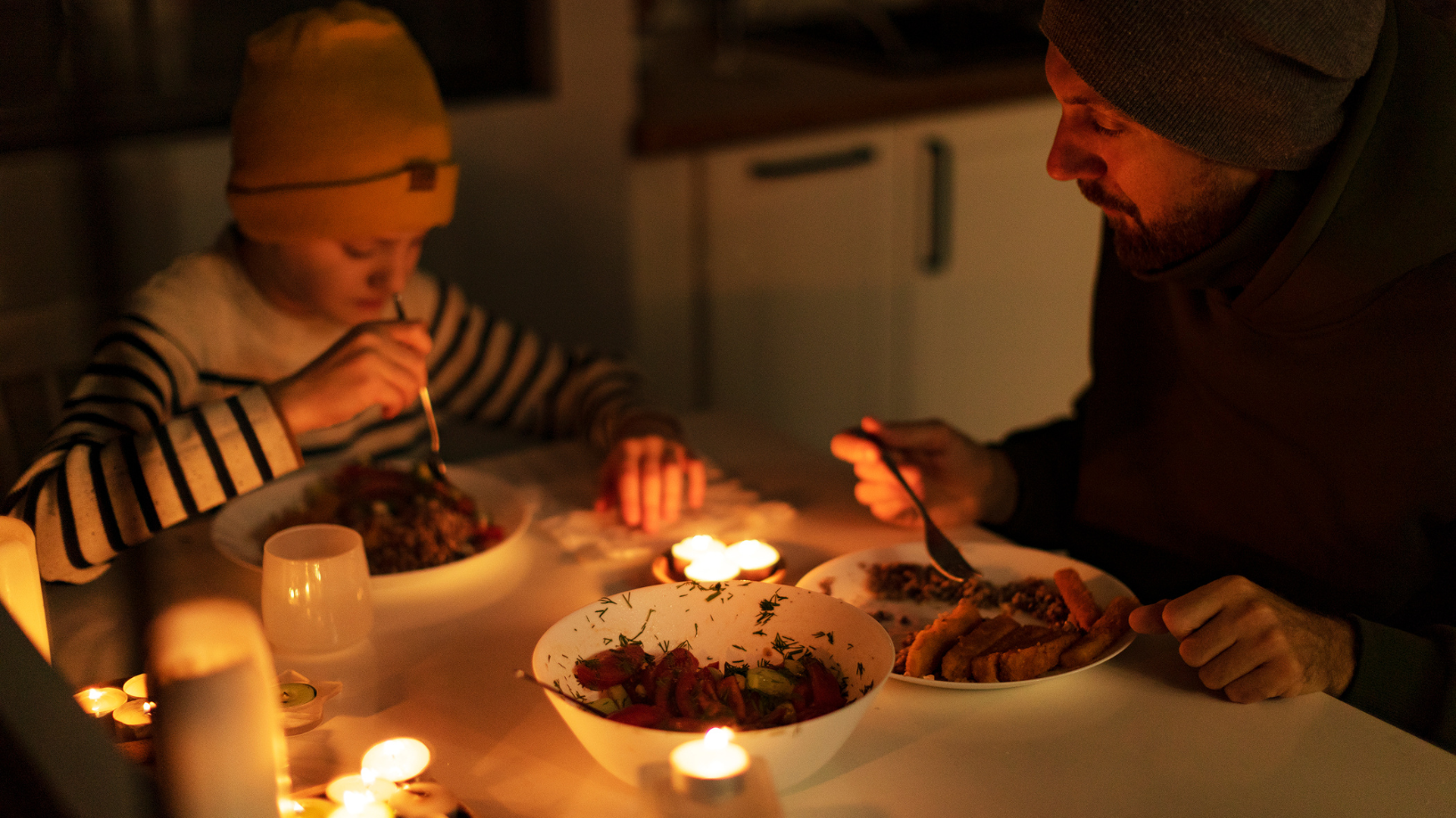 A father and son eat a meal in darkness apart from candle light. 