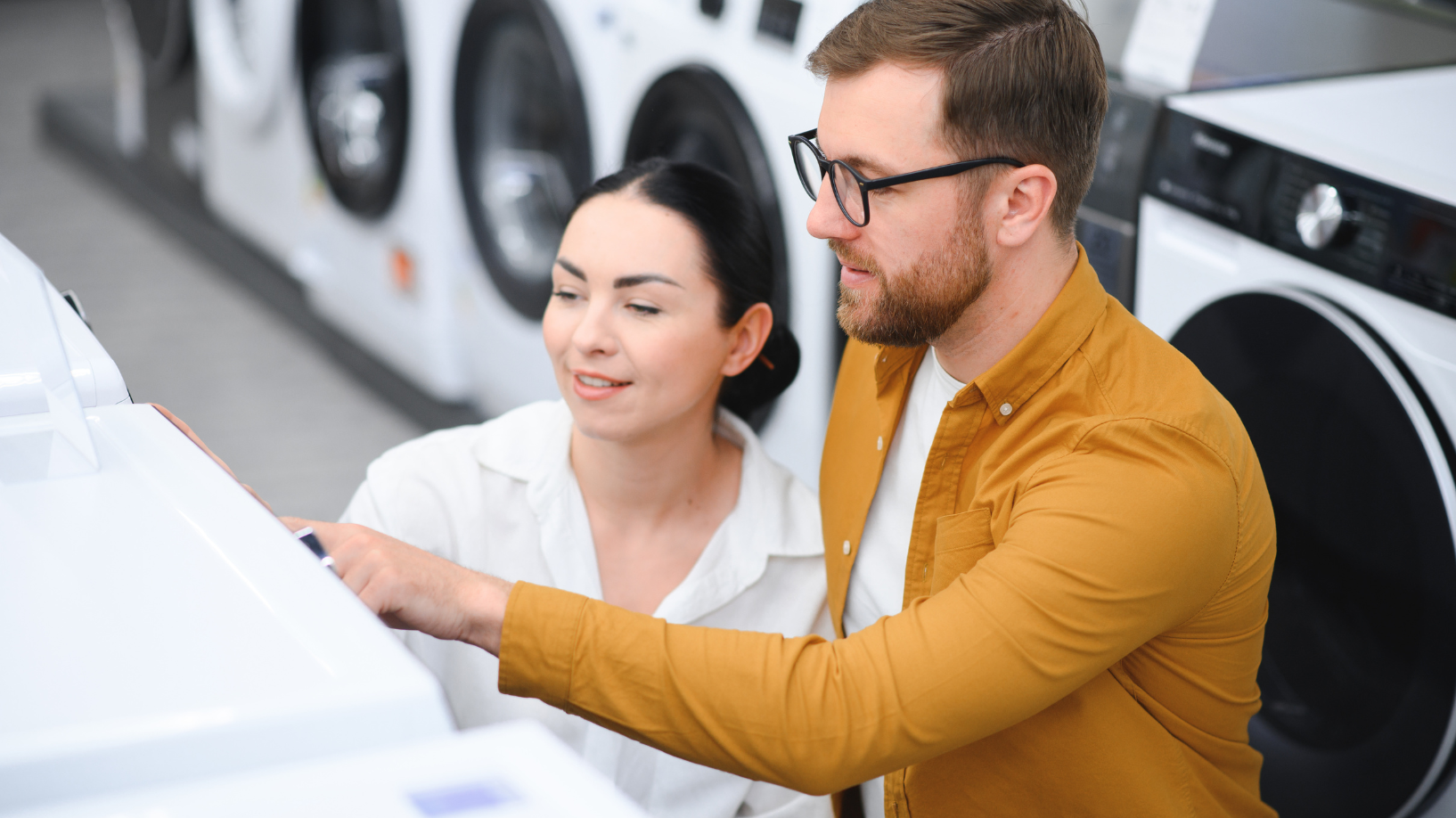 A couple is shopping and looking at washing machines. 