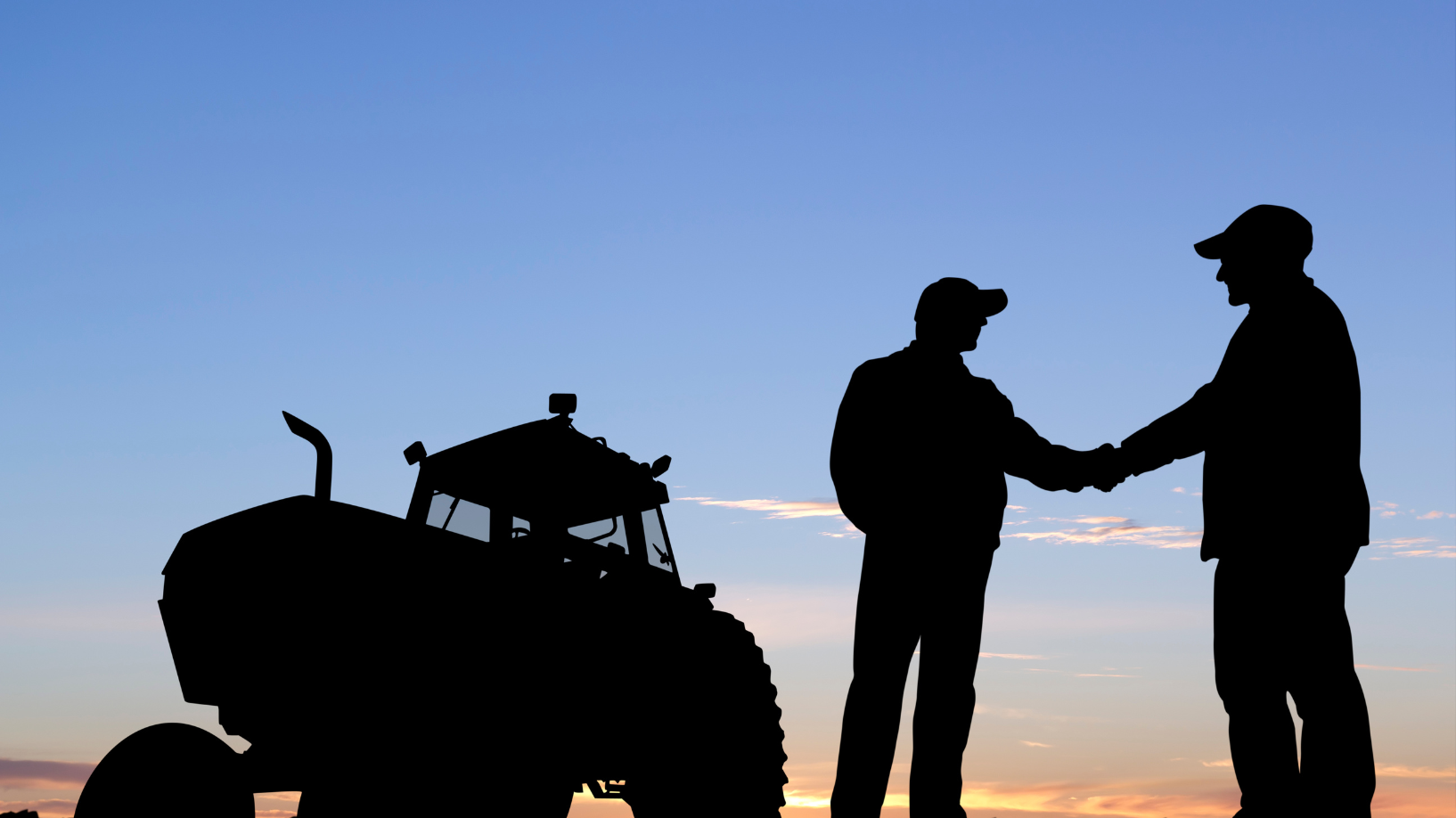 Two men shaking hands in front of a tractor. 