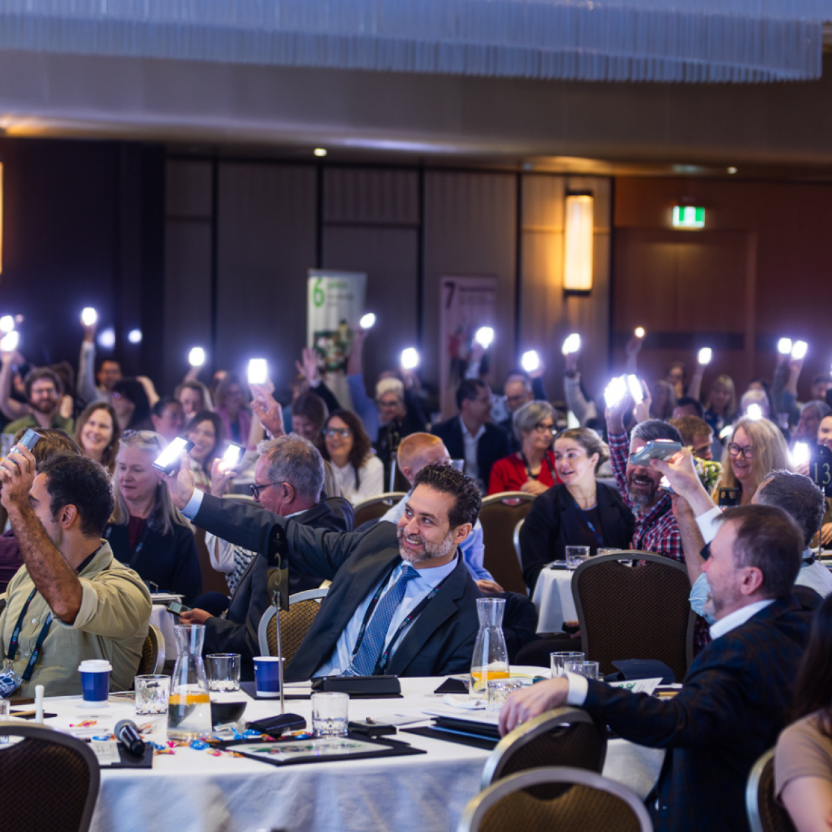 Photo of people in a large room, sitting at tables, holding up lights and smiling