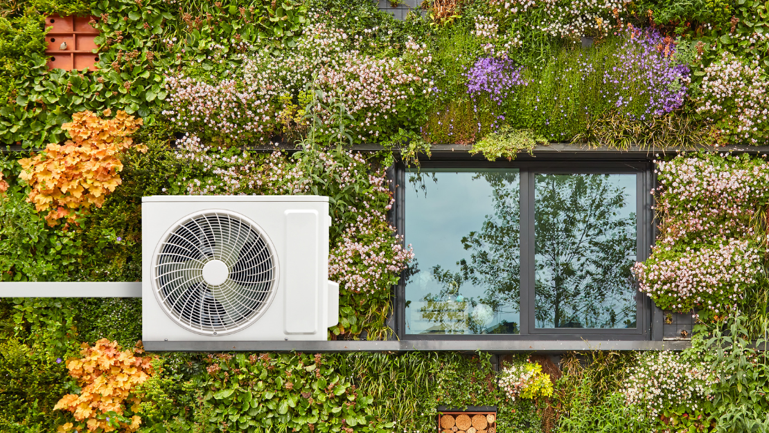 Photo of the exterior of a sustainable house, covered in flowers. A window and an air-source heat pump is in shot.