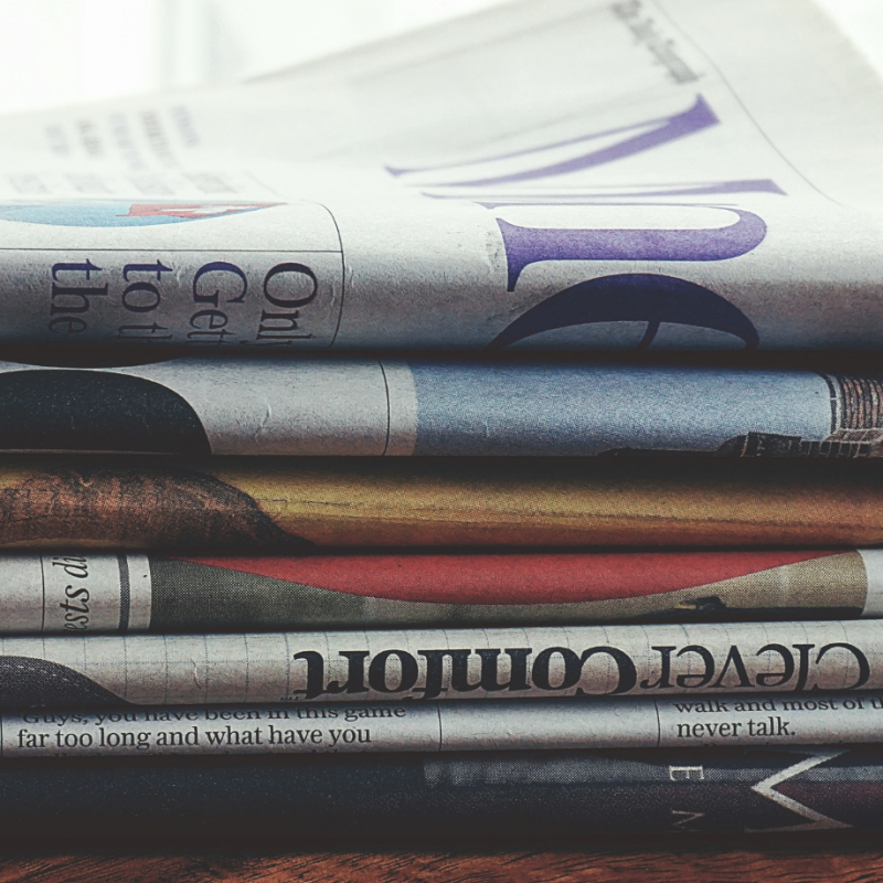 Photo of a stack of newspapers sitting on top of a wooden desk.