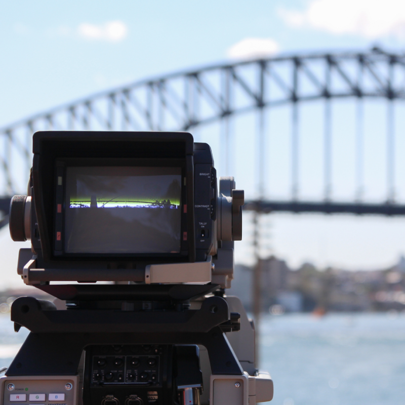 Photo of a news camera in front of the Sydney Harbour Bridge on a sunny day