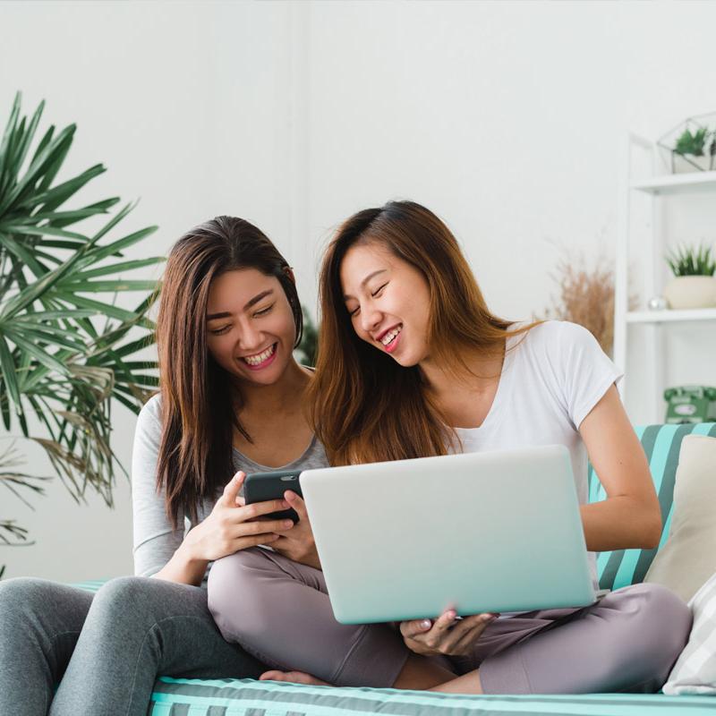Two young women sitting on a couch looking at a laptop