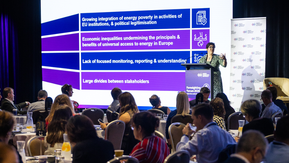 Photo of a presenter standing in front of an audience and a large screen at the 2026 Foresighting Forum.