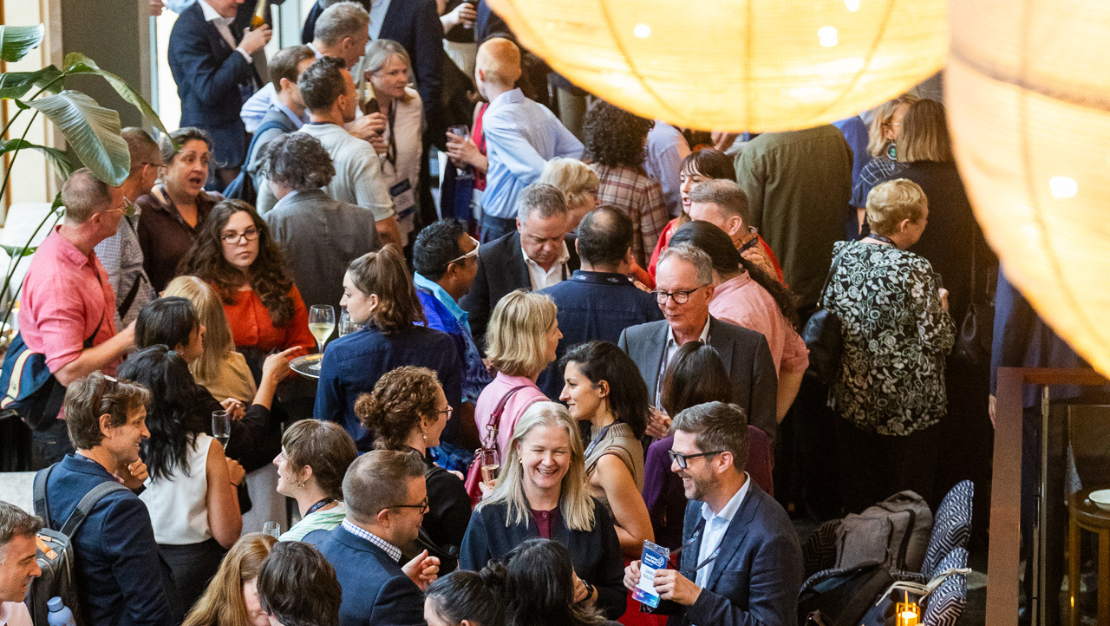 Photo of a crowd of people talking to each other, beneath large lights at the 2026 Foresighting Forum.