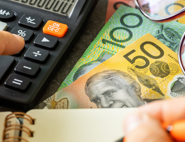Close-up photo of a hand with a calculator and Australian 50 and 100 dollar notes.