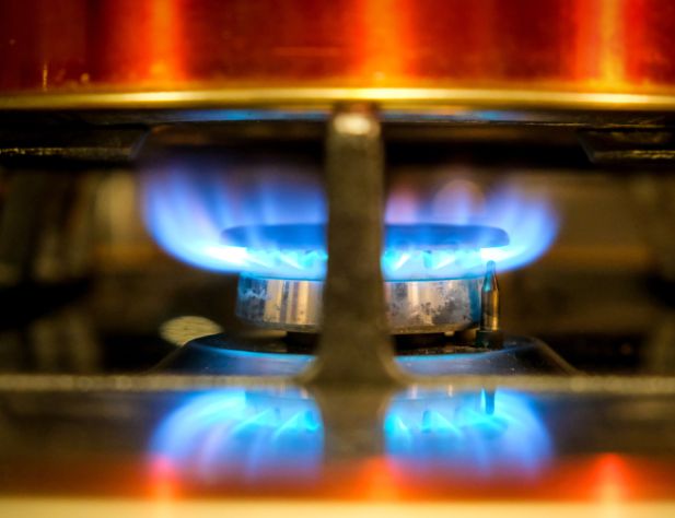 Close-up photo of a stovetop gas burner underneath a pot; the burner's flame is burning bright blue.