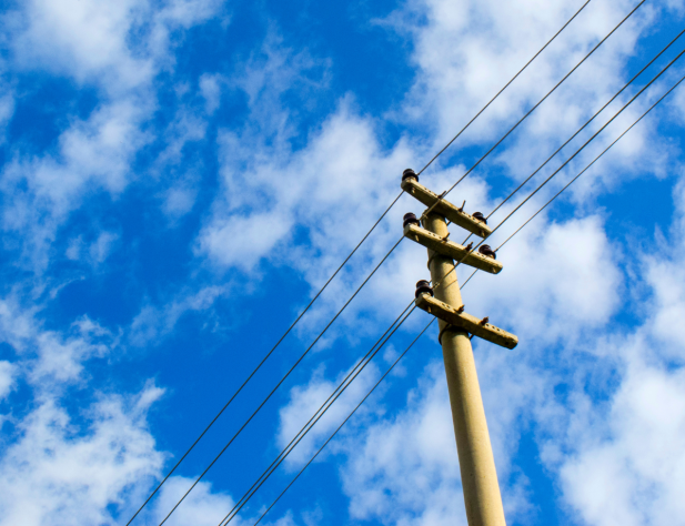 Photo of power pole against a blue sky with white fluffy clouds in it
