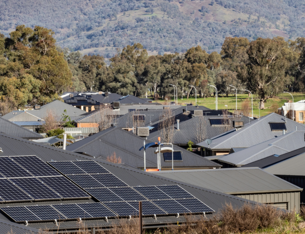 Photograph of rooftops in a rural Victorian neighbourhood, with gum trees in the background. The rooftop in the foreground has solar panels on it.