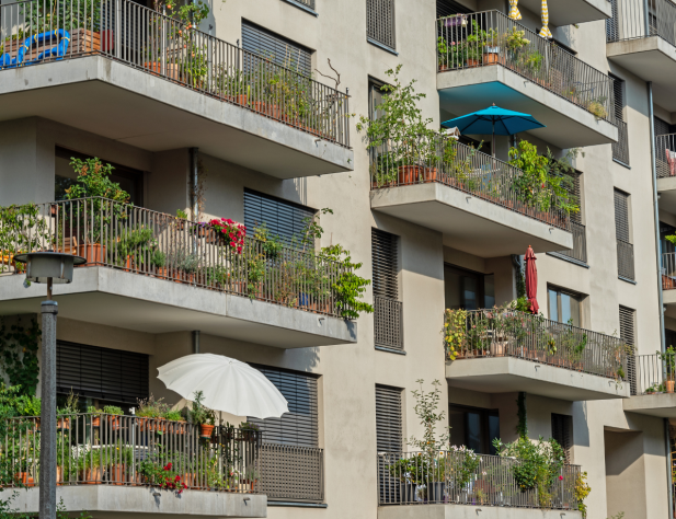Photo of an apartment block with lots of greenery and some umbrellas on its balconies