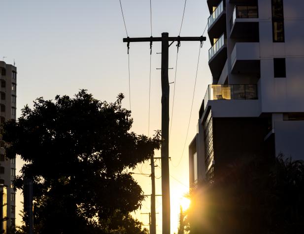 Photo of a power pole at dusk, next to a set of apartments and a tree.