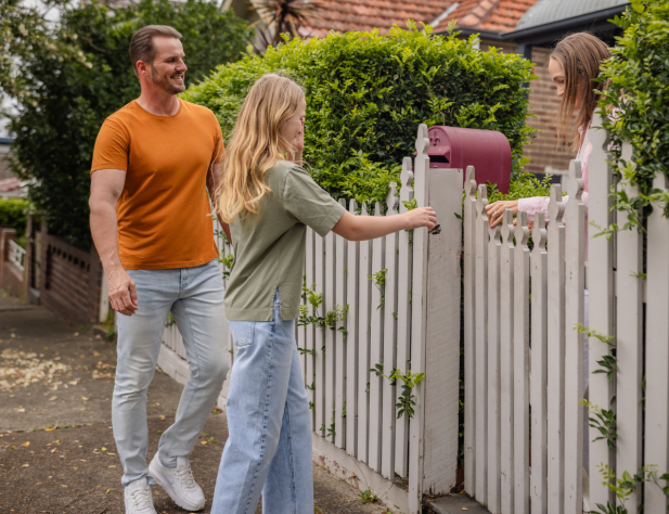 Photo of two people entering the front of a house with a white picket fence, via a gate