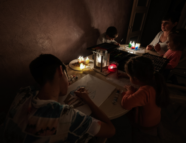 Family sitting at a table in the dark with candles illuminating their activities.