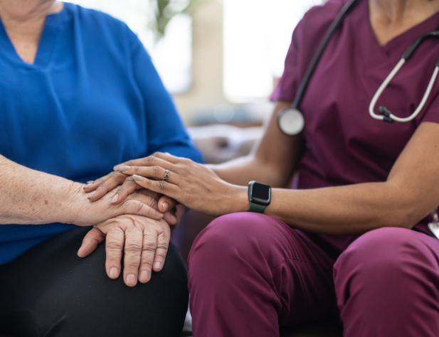 A doctor sits next to a patient and holds their hand.