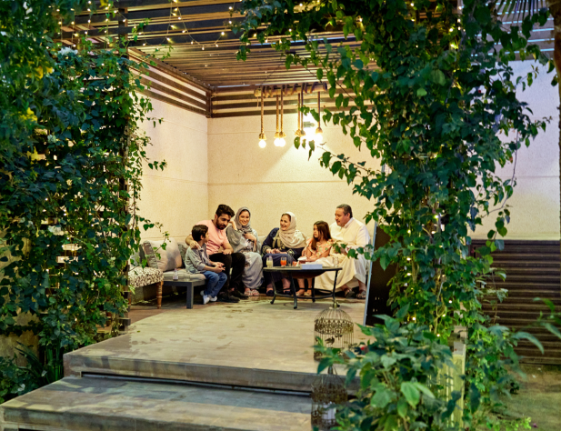 Photo of a family sitting on a patio underneath exterior lighting, surrounded by lush green plants.