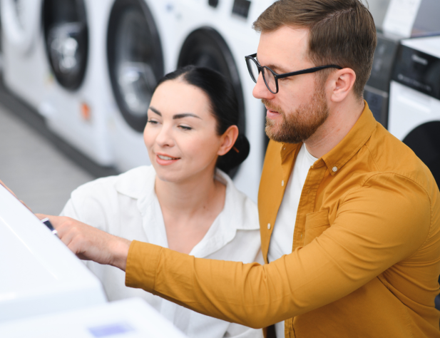 A couple is shopping and looking at washing machines. 