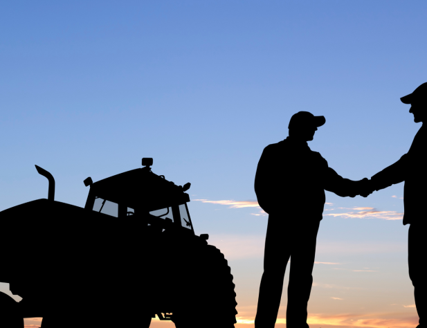 Two men shaking hands in front of a tractor. 
