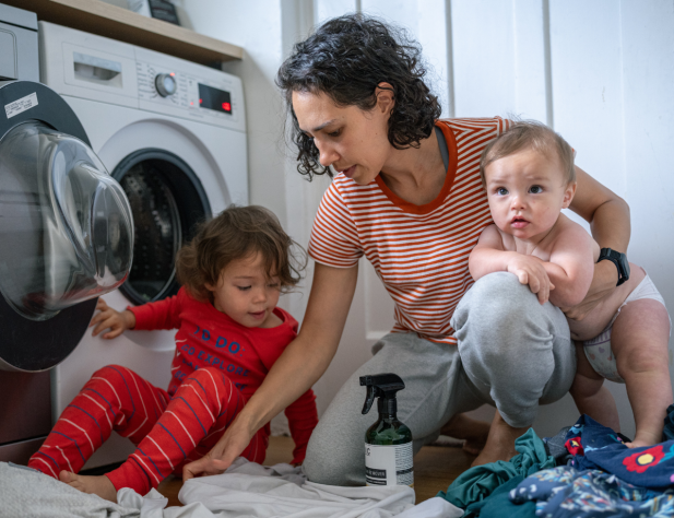Photo of a woman sorting through washing in front of a washing machine, accompanied by two small children