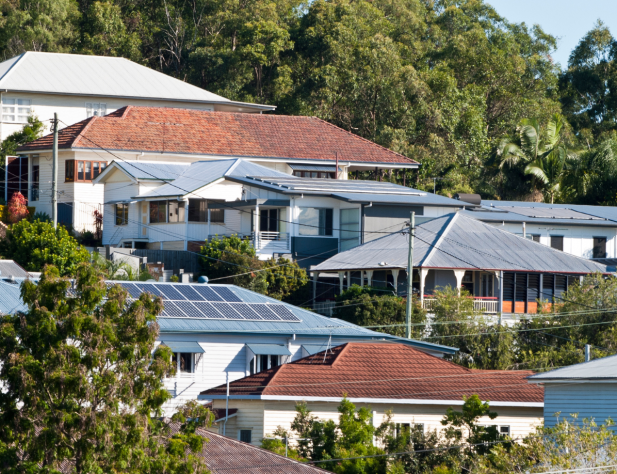 Photo of a row of houses in a sloping Queensland street, surrounded by trees. Some houses have rooftop solar, and are connected to the electricity network.