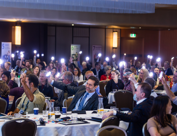 Photo of people in a large room, sitting at tables, holding up lights and smiling