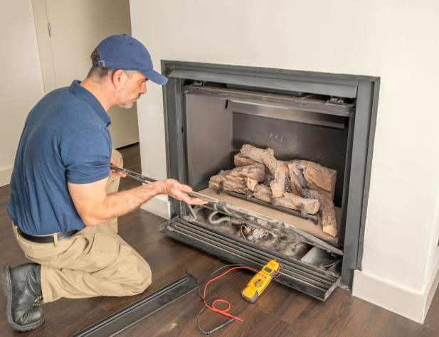 Photo of an interior space with a crouching tradesperson, who is fixing a gas fireplace.