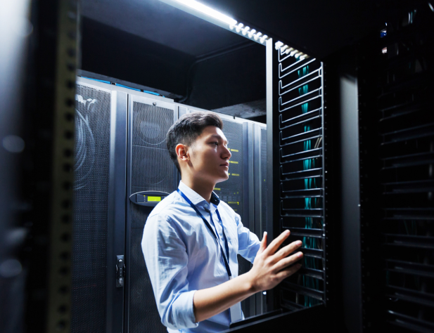 Close-up photo of a person in a blue shirt inspecting a server in a lit-up room.