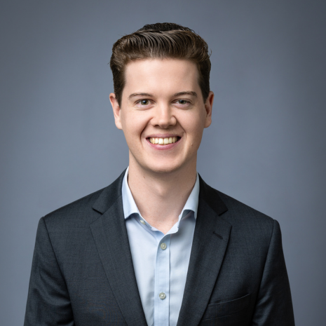 Photo of a person in a suit looking at the camera, smiling.