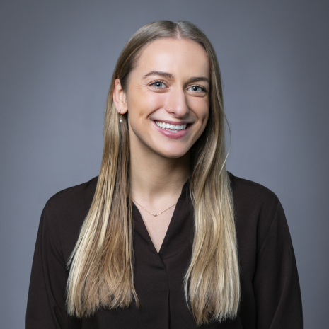 Photo of a person with long blonde hair, wearing a dark shirt, looking at the camera and smiling.