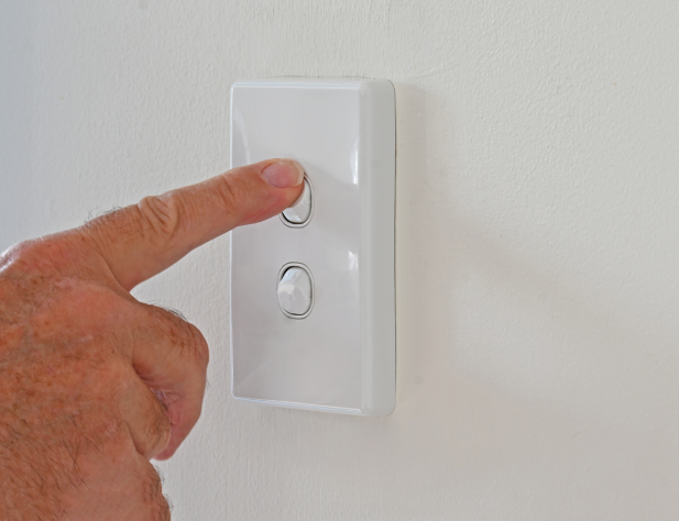 Photo of a hand pressing a shiny white light switch on a white wall.