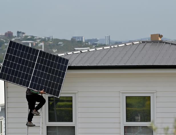 Photo of a person with a solar panel, standing on a ladder. They are going to install the solar panel on a rooftop.