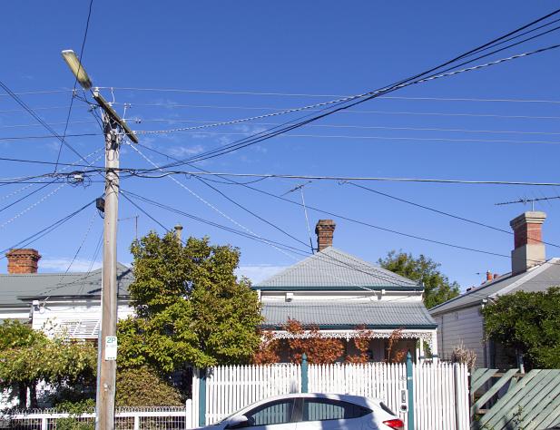 Photo of an Australian urban street, in which you can see a power line supplying power to the three houses in shot. It is sunny and there is a bright blue sky in the background.