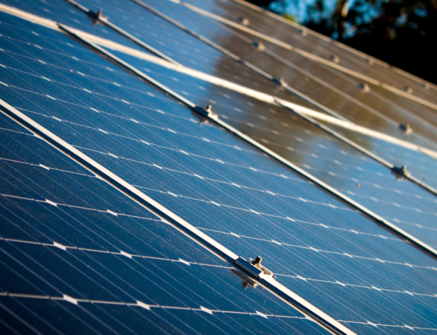 Close-up photo of solar panels with sky and trees reflected on them.