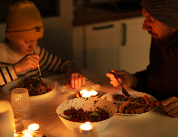 A father and son eat a meal in darkness apart from candle light. 