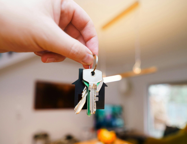 Photo of a hand dangling keys in the foreground, with the interior of a property in the background.