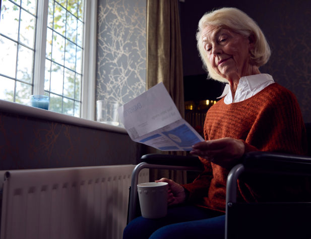 Photo of a woman reading an energy bill, sitting in a wheelchair, next to a window