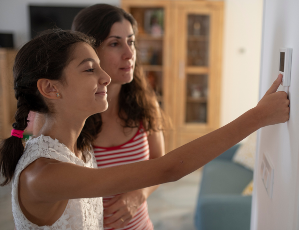 Photo of two people using a thermostat in a home interior