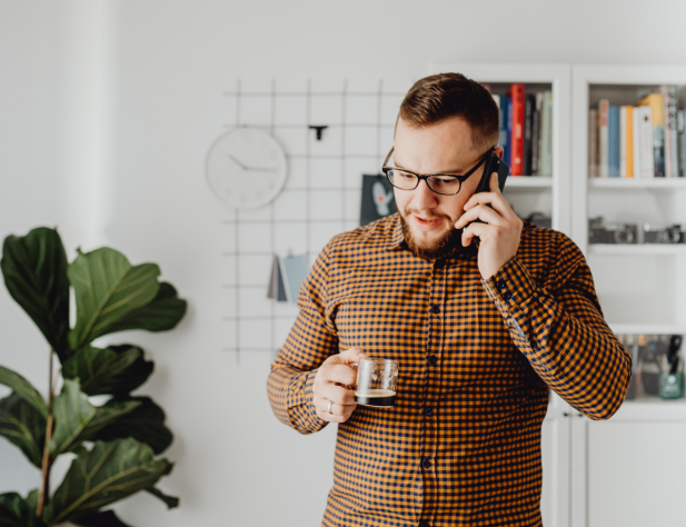 Photo of a person in an interior setting, using a phone and holding a cup of coffee.