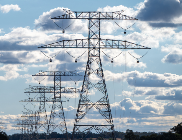 Photo of transmission towers against a blue sky filled with clouds, in an Australian rural landscape.